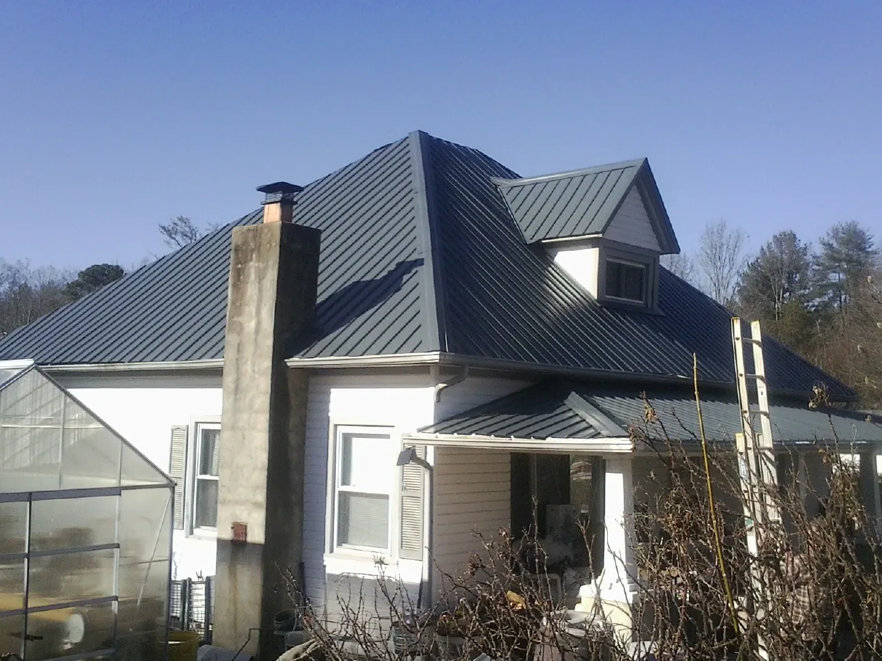Dark blue standing seam metal roof on a white farmhouse with dormer — Slate & Tile Roof Repair by Roofing Brothers in Hartline