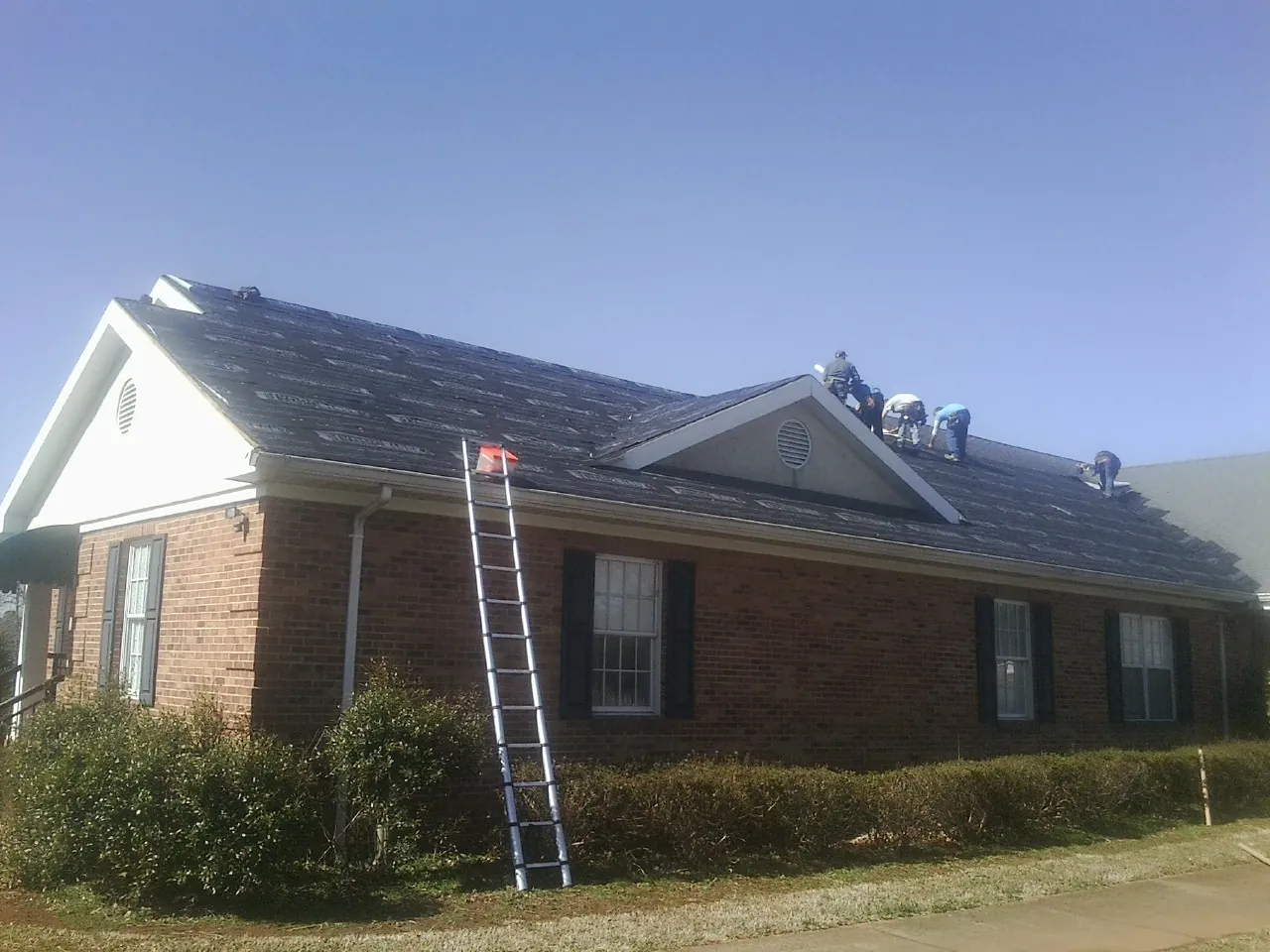 Crew tearing shingles off a brick ranch roof with a ladder set — Emergency Roof Repair work by our crew in Hartline