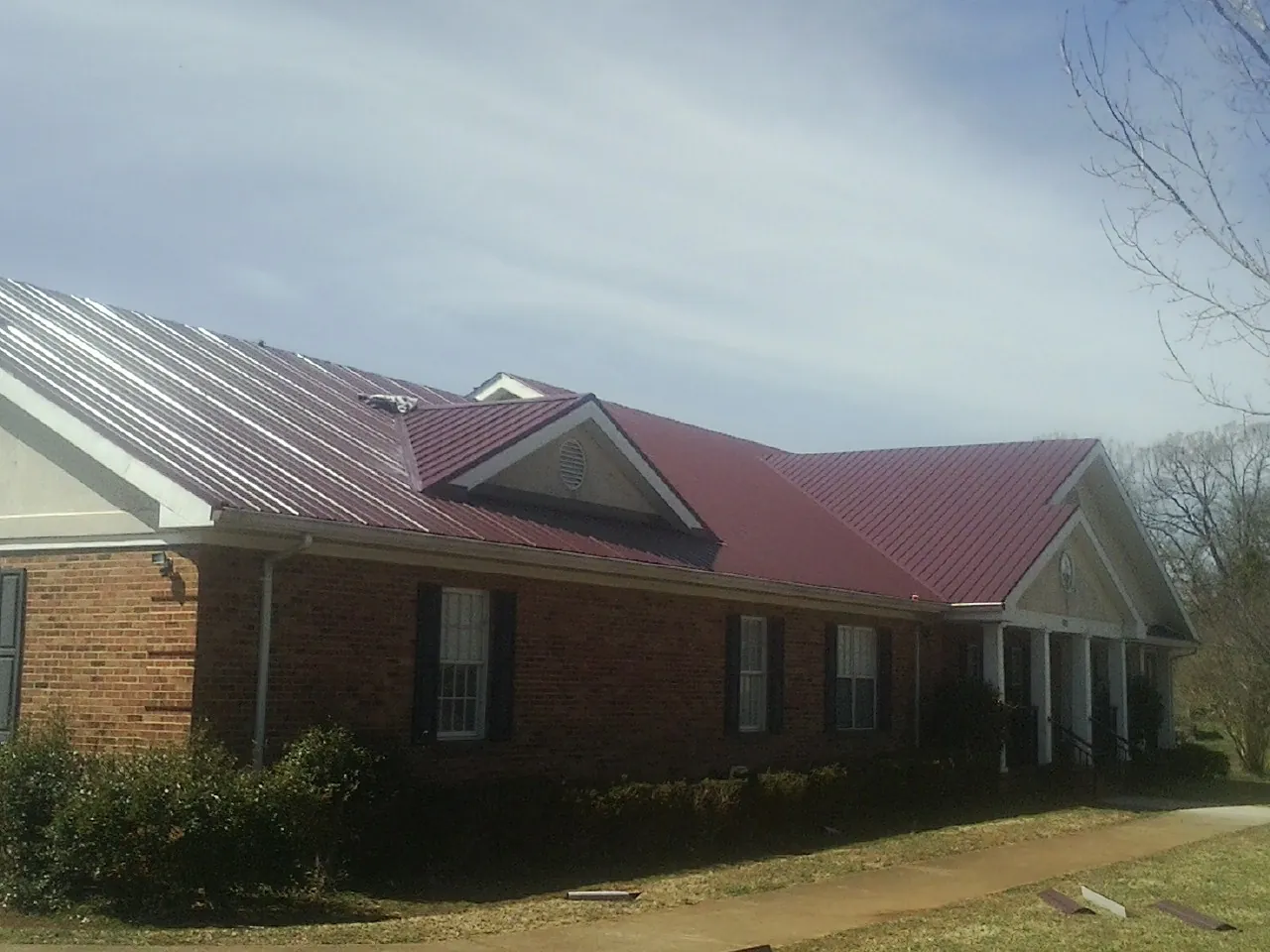 Red metal roof with gabled entries on a long brick building, from a Hail Damage Roof Repair job in Hartline