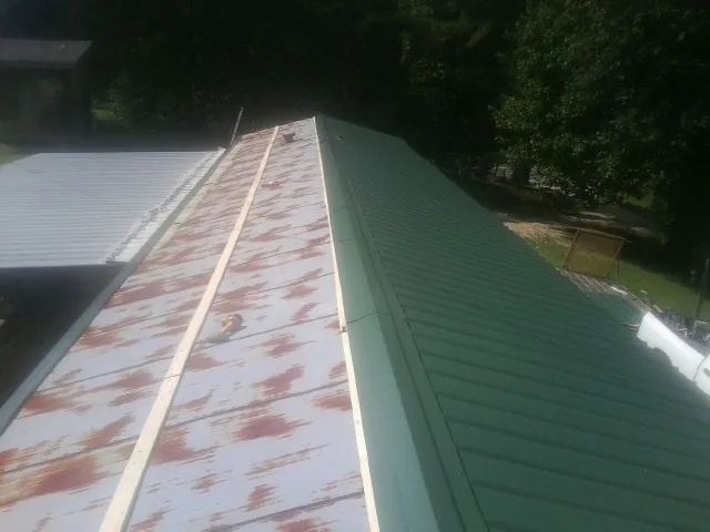 Old rusted panels beside newly installed green metal roofing — Wind Damage Roof Repair by Roofing Brothers in Hartline