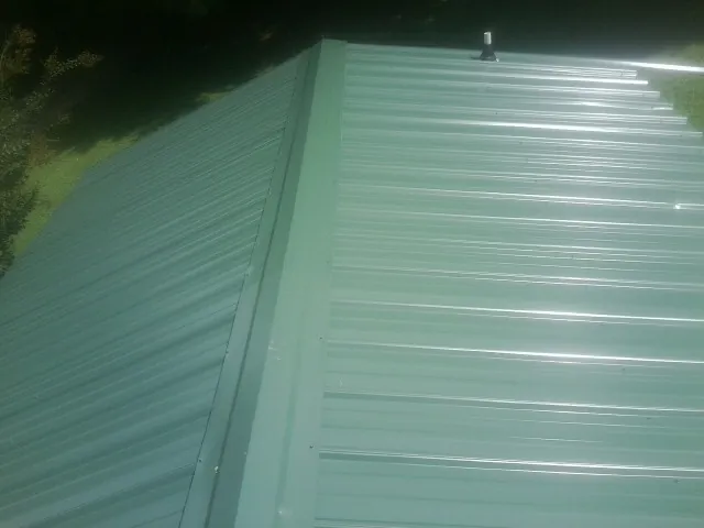 New green metal panels meeting at the ridge of a roof — Flat Roof Repair work by our crew in Hartline