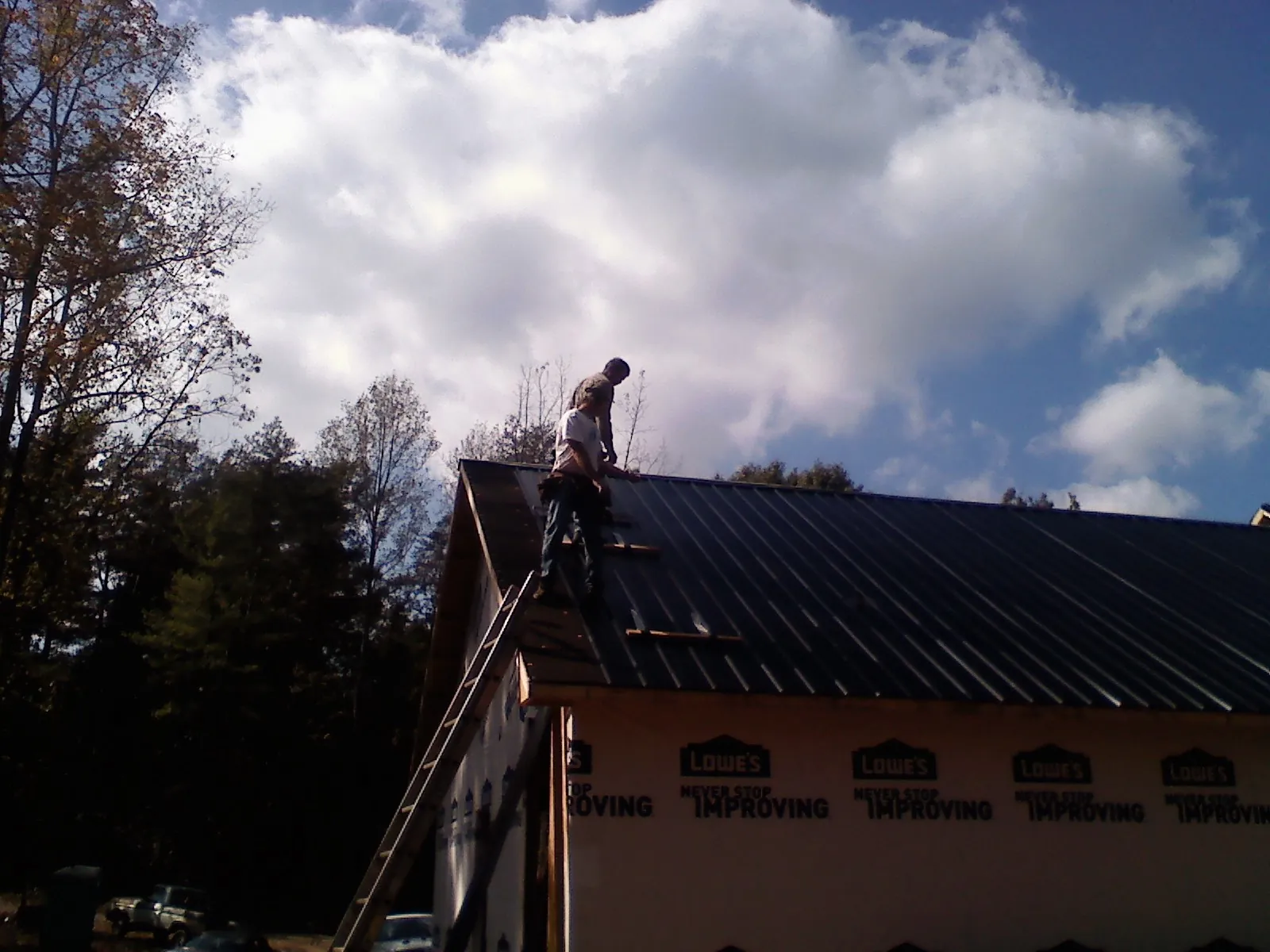 Roofer fastening dark metal panels high against a cloudy sky, from a Roof Inspection job in Hartline