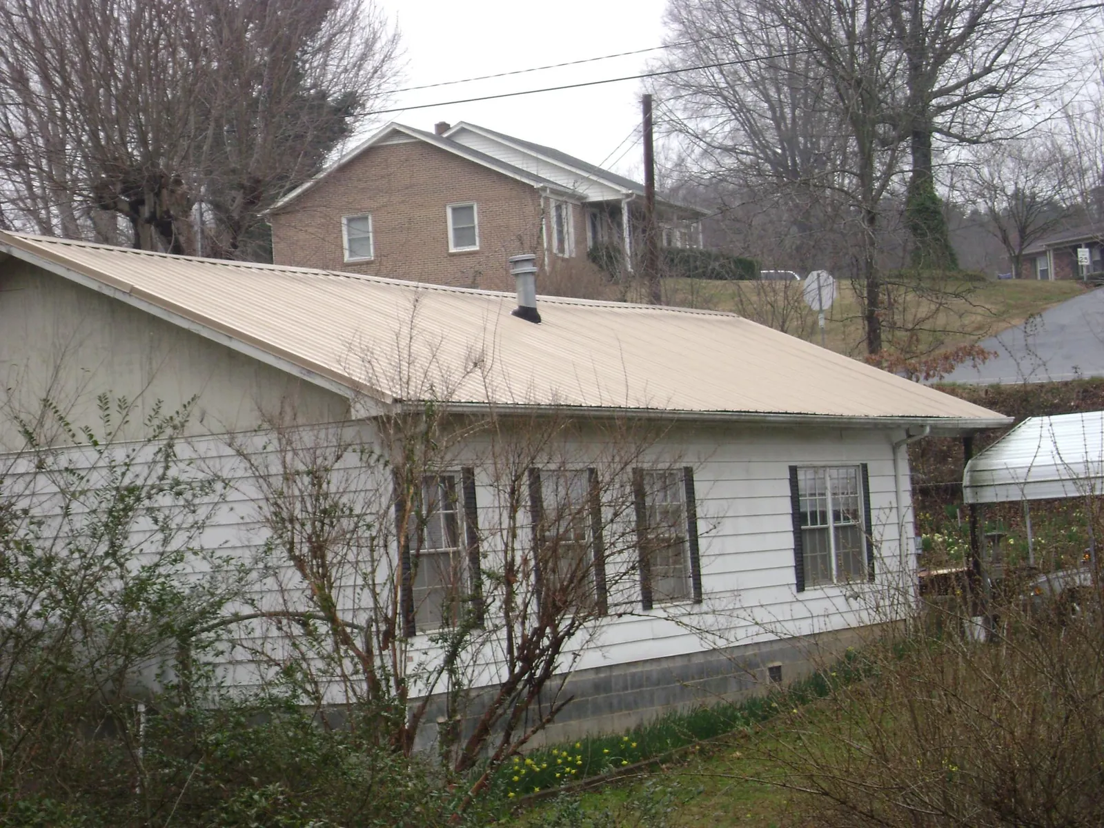 Tan metal roof on a white sided house set into a hillside — Commercial Roofing by Roofing Brothers in Hartline