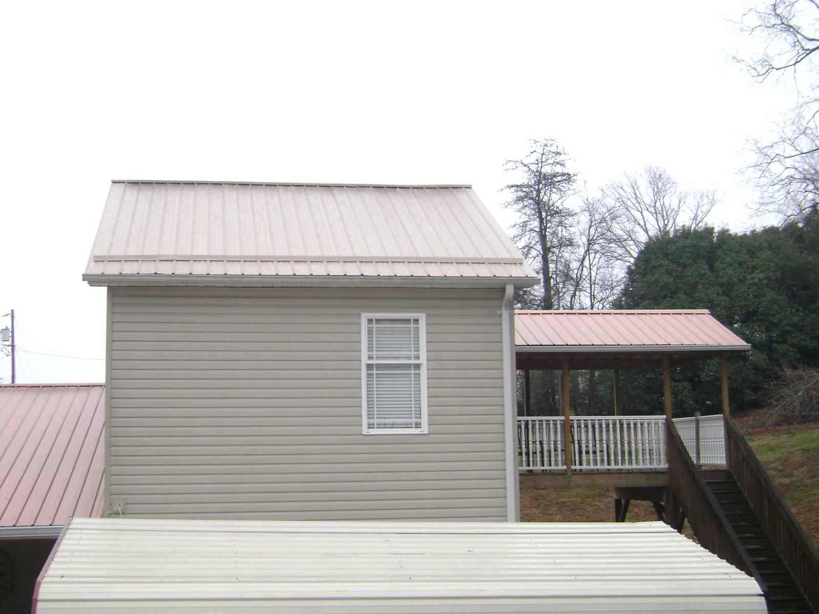 Tan metal roofs on a two story addition and attached porch, from a Roof Replacement job in Hartline